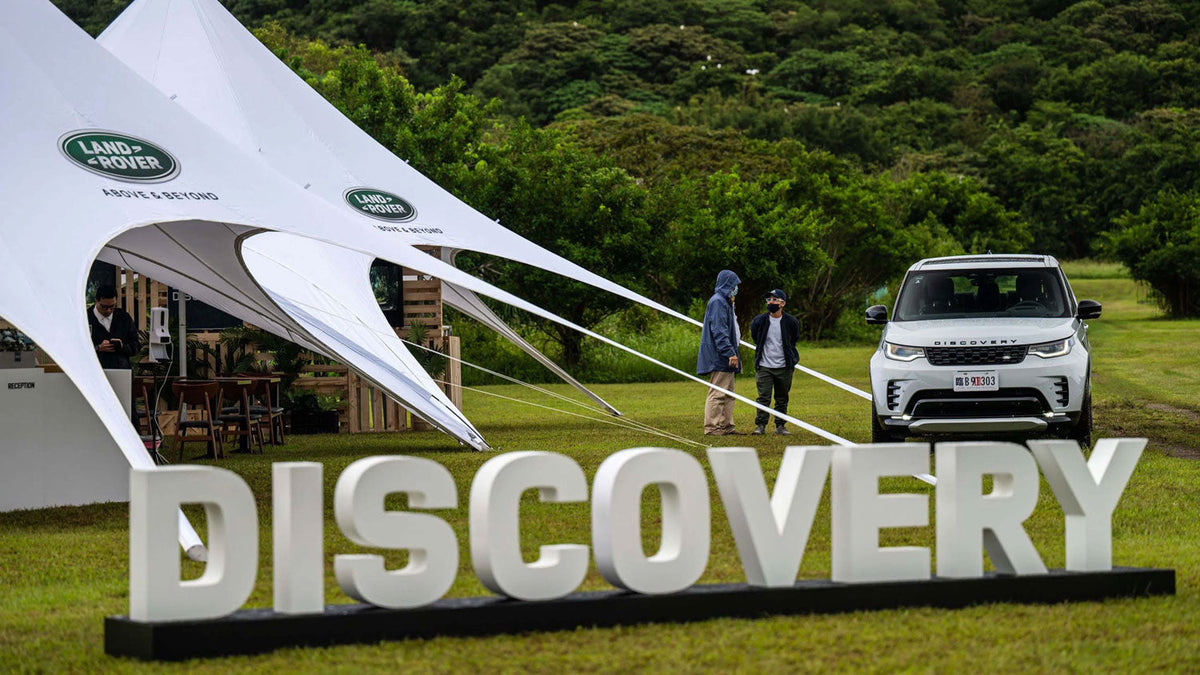Evenement met grote witte tenten met het Land Rover-logo "Above & Beyond", opgezet op een grasveld omringd door bossen.