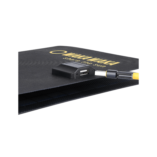 Een opvouwbaar zwart zonnepaneel met het WakaWaka-logo en de tekst “share the sun”, met een aangesloten kabel en USB-poort zichtbaar aan de rand, tegen een transparante achtergrond met ruitpatroon.