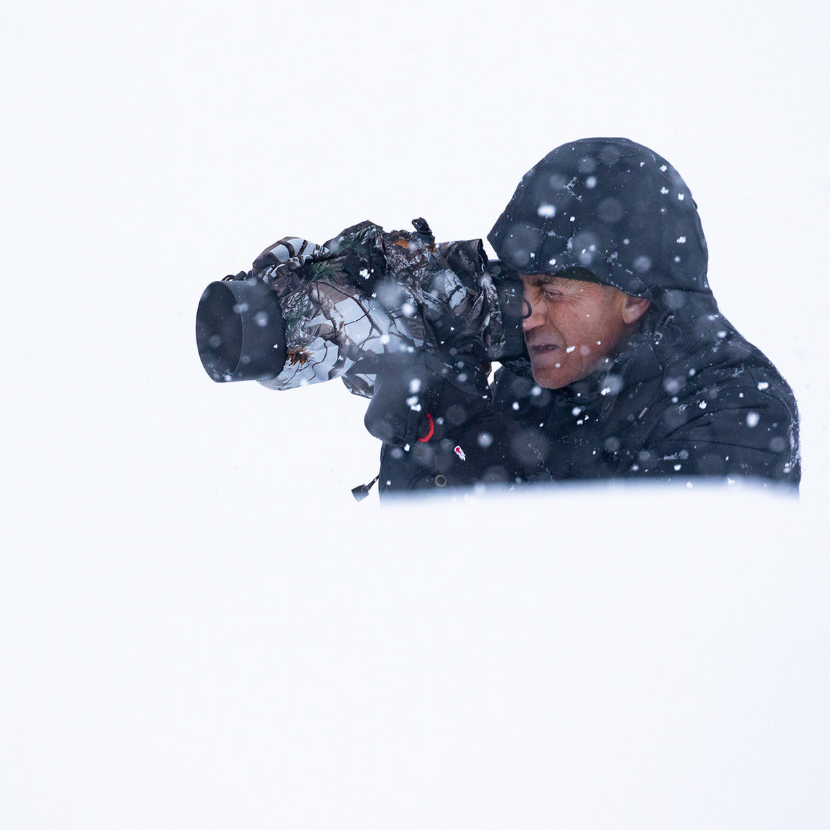 Housse de pluie Buteo 1 en utilisation, photographe avec appareil et objectif sous la housse dans la neige