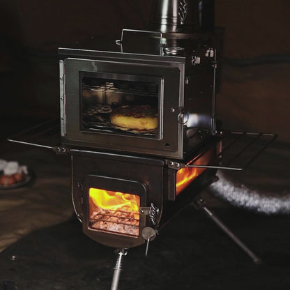 compacte camping houtkachel met geïntegreerde oven, glazen kijkvensters en zichtbare vlammen, terwijl een pizza bakt in de bovenste ovenruimte binnen een tentomgeving