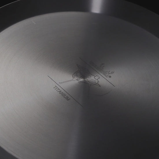 close-up van de binnenkant van een titanium koekenpan met gegraveerd logo en tekst in het midden