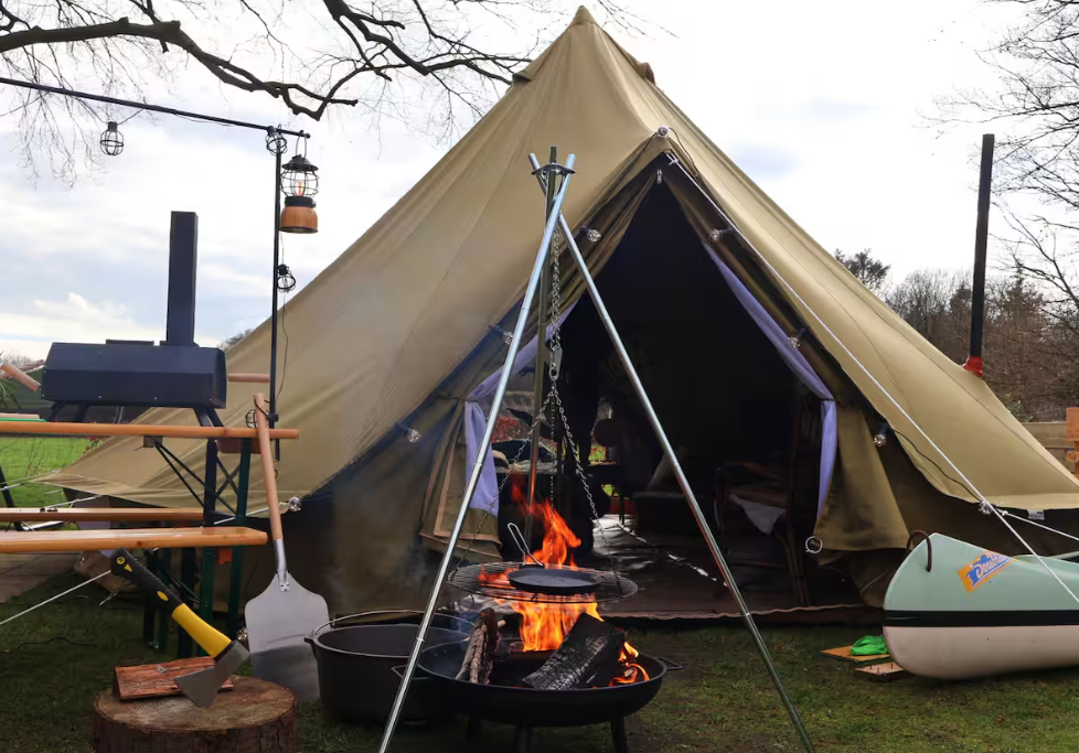 Groene Sibley ProTech 500 tent van CanvasCamp op de proefslaaplocatie bij Camping Zwolsedijk met een brandend kampvuur, kookdriepot, kano en buitenkeuken ervoor.