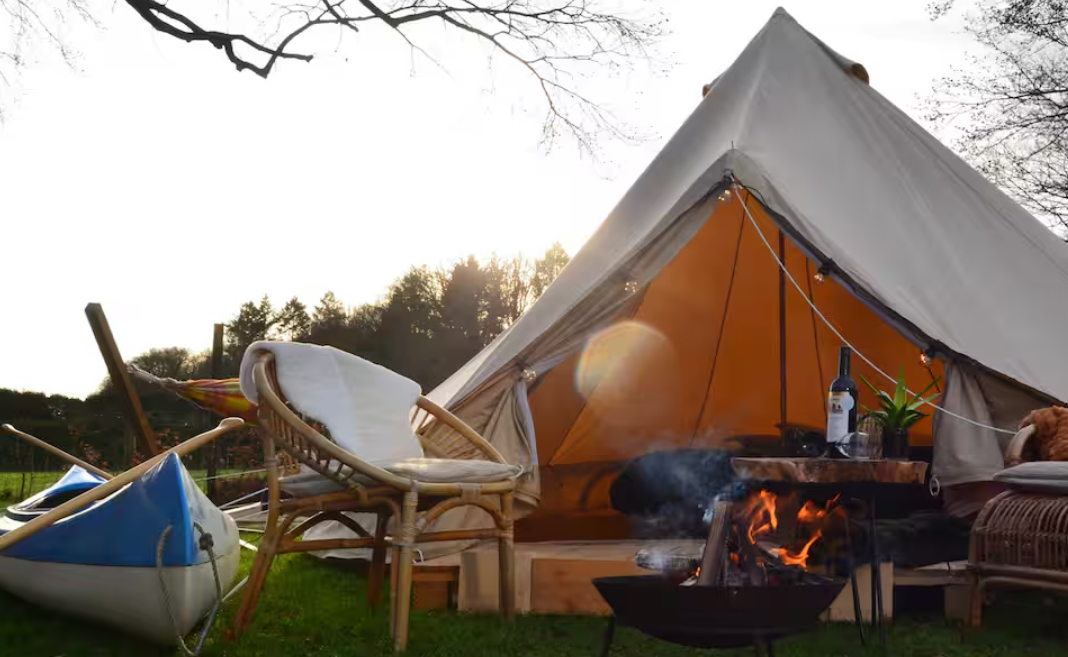 Proefslaaplocatie bij Camping Zwolsedijk met een Sibley ProTech 500 tent van CanvasCamp aan het water, rieten stoelen, een kano en een brandend kampvuur ervoor.